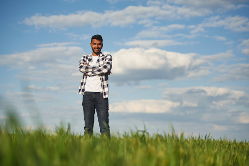 Cloudy sky on background. Handsome Indian man is on the agricultural field.