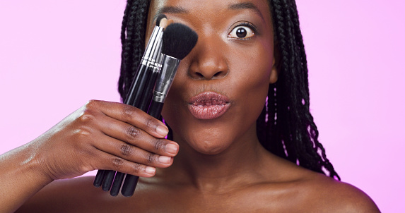 Makeup, beauty and portrait of black woman with brush on purple background for cosmetics in studio. Cosmetology, surprise and happy female person with brushes for foundation, face powder and contour