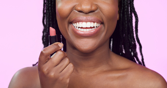 Makeup, smile and black woman with lipstick in hand, happiness and cosmetic product on pink background. Cosmetics, beauty and skincare, happy model with lips and color application on mouth for shine.