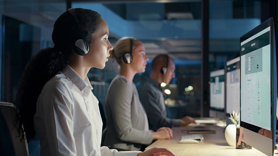 Call center agents talking, making conversation and helping people online while working late in an office. Customer service agents advising, networking and client answering questions during overtime