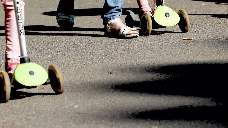 feet of passers-by walking on asphalt and feet of children with scooters on a sunny day