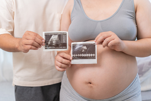 Asian pregnant woman with Thai husband at home. Love couple together and unborn baby. Family lifestyle.