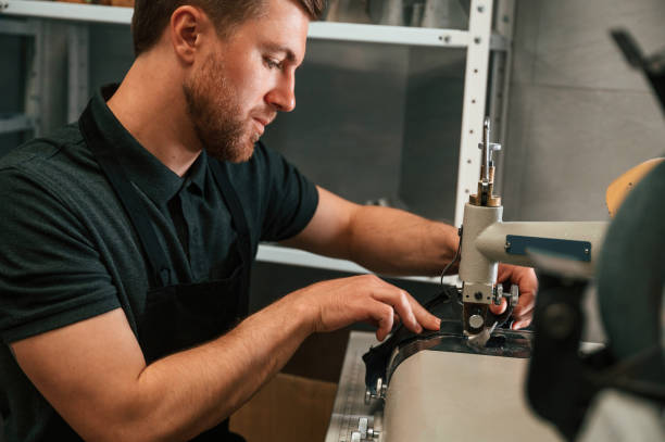 istock View from the side. Working by sewing machine. Man in black shirt is indoors 1497877837