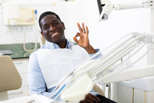 Portrait of positive man making ok gesture, sitting on dental chair Portrait of positive african-american man sitting on dental chair, making ok gesture and smiling. kenyan man stock pictures, royalty-free photos & images