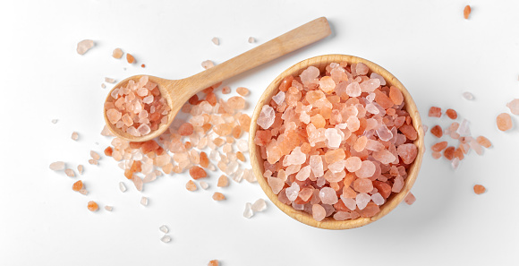 Himalayan pink salt in wooden bowl with spoon on white background, top view