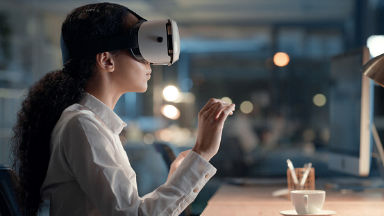 Businesswoman wearing VR headset to connect and interact in a metaverse with a digital user interface in an office at night. Entrepreneur in an immersive virtual world with AI and 3D simulations