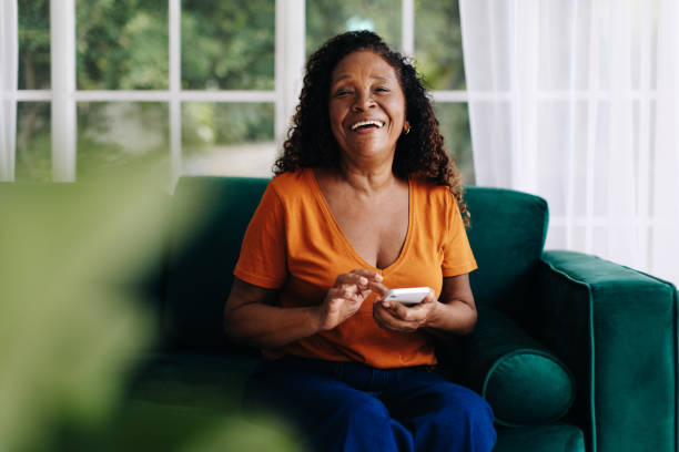 Happy black woman enjoying using mobile apps for seniors on her smartphone Joyful and tech-savvy black woman in her golden years enjoys exploring mobile apps tailored for seniors, connecting with others, and enhancing her lifestyle through her smartphone. senior women stock pictures, royalty-free photos & images