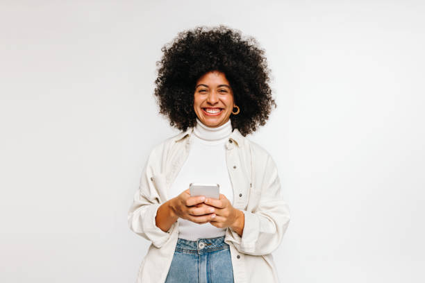 istock Cheerful young woman smiling at the camera while holding a smartphone 1497885890