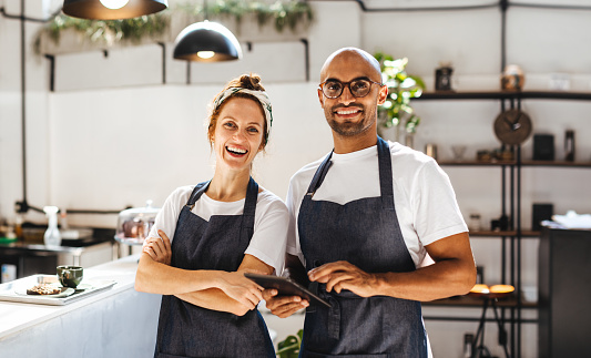 Two hospitality entrepreneurs standing confidently in their small coffee shop. Successful man and woman working as a team to manage the day-to-day operations and provide excellent service to their customers.