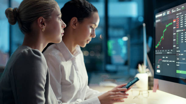 istock Finance business women talking and looking at data, stats and a graph on a computer screen while working late at night in an office. Female colleagues analysing a chart and trading stock online 1497891443