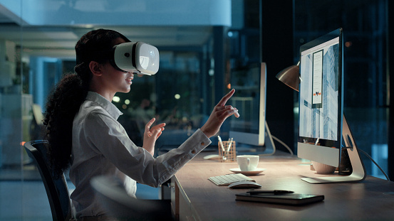 VR headset and goggles of a young woman testing a new tech project on a office computer. Modern technology creator test futuristic 3d virtual meeting. Female digital worker talking to people online