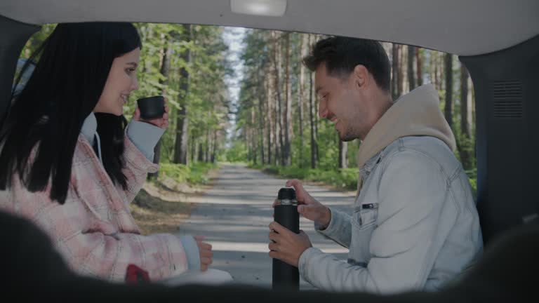 Slow motion of young couple tourists drinking tea from thermos sitting in car enjoying vacation