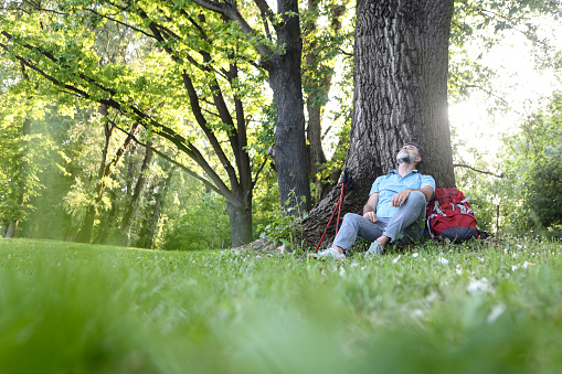 Mature man hiking in nature, relaxing by a tree. About 55 years old, Caucasian male.