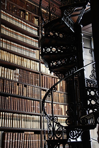 A Spiral staircase in an old library. Located in the heart of Trinity College University in Dublin, Ireland, the Old Library is the oldest library in the city. Built in the 18th century, it contains thousands of books spread over 2 floors, in a warm decor made of woodwork and vaults