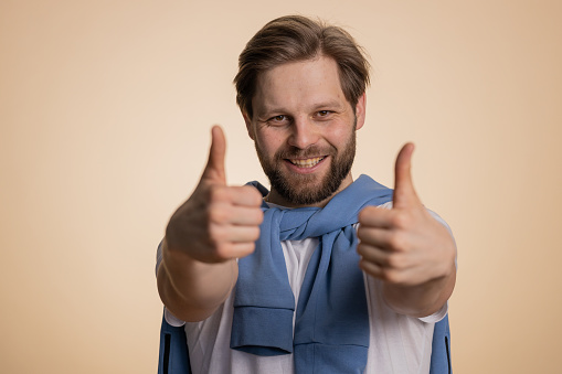 Like. Caucasian young man in t-shirt raises thumbs up agrees with something, gives positive reply recommends advertisement likes good. Handsome bearded guy isolated alone on beige studio background