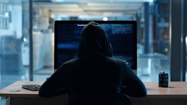 istock Back of hacker or cyber criminal stealing information online sitting at a computer at night. Hooded mysterious person coding spyware, malware and viruses to commit fraud, theft and phishing scam 1497901171