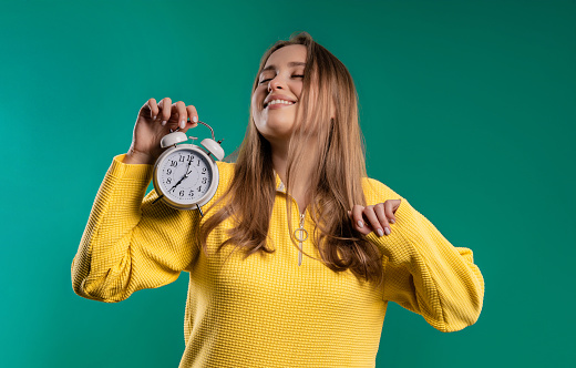 Happy lady with alarm clock on teal background. Early morning, correct day routine, living in moment, appreciate every minute of life, youth. High quality