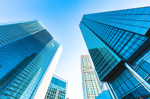 Wide angle color image depicting a businessman, mainly in silhouette and unrecognisable, walking in his office building. The interior architecture is ultra modern and abstract, full of leading lines, glass and reflections. The businessman is walking towards the camera, while carrying a shoulder bag and an umbrella. Room for copy space. ***image taken in City Hall, London, UK, a publicly owned building freely accessible to the public without entry fees or photographic restrictions***