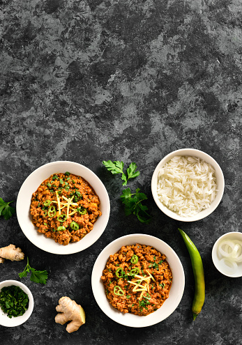 Keema curry and rice in bowls over dark stone background with free space. Indian and pakistani style dish. Top view, flat lay