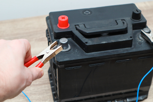 Close up of hand Charging car battery with electricity trough jumper cables. Electrical charging Cables on a 12 volt Battery