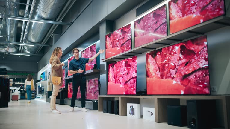 Hispanic Woman Having a Conversation with Home Electronics Store Associate. Young Multiethnic Customer Pursues Cutting-Edge TV Technology. Shopper Examining Modern Television Selection in a Showroom