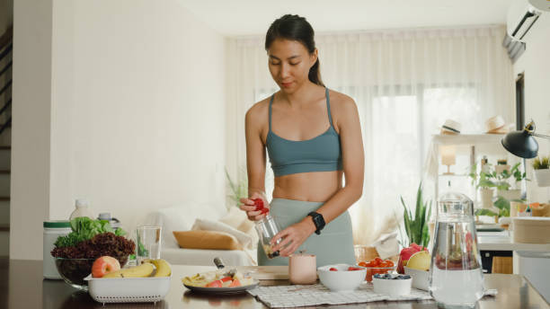 young asian athletic woman using blender and preparing fresh fruit smoothie at home. healthy food. - routine foods and drinks clothing household equipment imagens e fotografias de stock