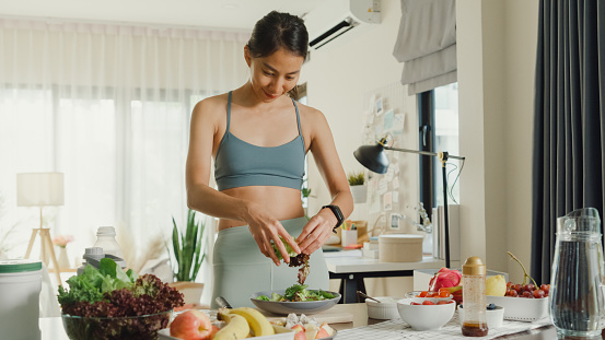 Young Asian athletic woman cooking salad at home. Diet and healthy food concept.