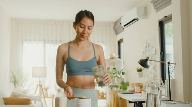 Young Asian athletic woman preparing protein shake at home. Diet and healthy food. Young Asian athletic woman preparing protein shake at home. Diet and healthy food concept. bodybuilding supplement stock pictures, royalty-free photos & images