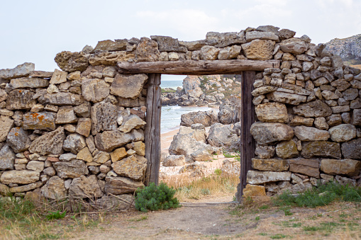 An old dilapidated stone wall with a doorway overlooking the sea and the rocky shore. Film decoration.