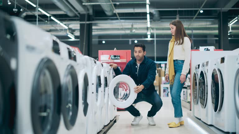 Multicultural Couple Evaluates Washing Machine Choices at Home Electronics Store. Man and Woman in Search of a Reliable Laundry Appliance. Customers Explore Modern Laundry Solutions in a Retail Shop