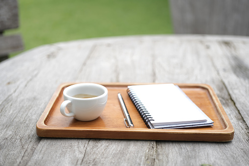 White coffee cup on wooden table with notebooks on wooden tray on grunge wooden table