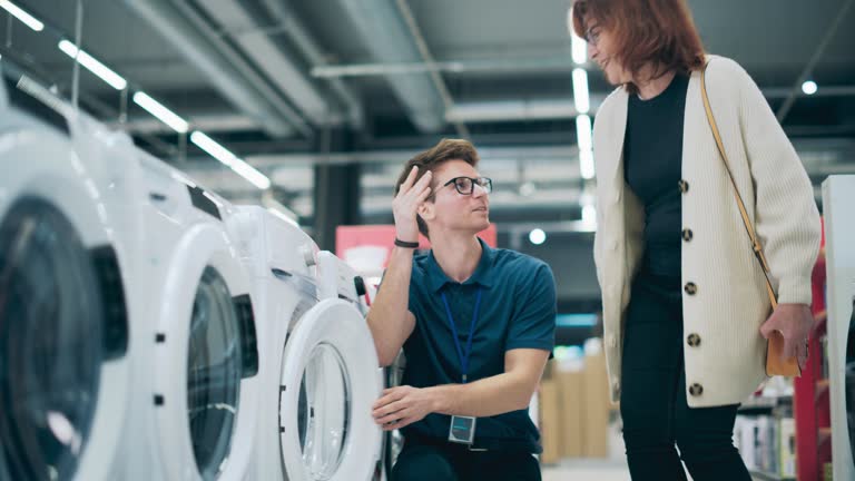 Portrait of a Senior Female Customer Seeking Expert Advice from Retail Home Electronics Expert for Washing Machine Purchase. Woman Explores Contemporary Laundry Appliance Options in a Department Store