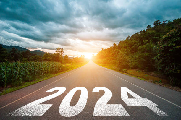 2024年の新年のコンセプト。日没時にアスファルト道路の真ん中の道路に書かれたテキスト2024。計画、目標、課題、新年の抱負のコンセプト。