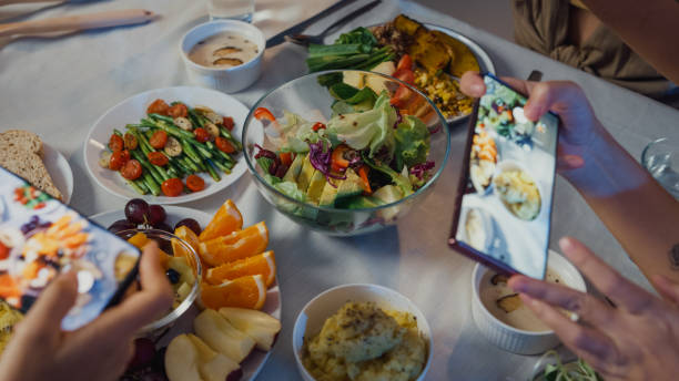 Close up of young Asian women friends talking fun and taking a photo of food sit at dining table in dining room at home at night. Lifestyle healthy food eating enjoy life and plant-based diet concept. primer plano de jóvenes amigas asiáticas hablando de diversión y tomando una foto de comida sentada en la mesa del comedor en casa por la noche. estilo de vida alimentos saludables comer disfrutar de la vida y la dieta basada en plantas.