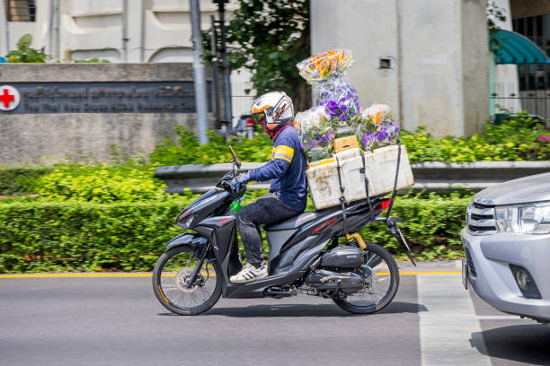 Bangkok, Thailand - March 27th 2023: Man with flowers driving down a road on a motorcycle in the center of the capital of Thailand