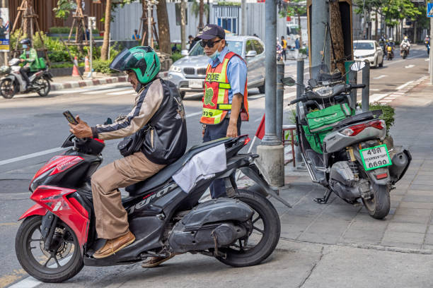 Bangkok, Thailand - March 24th 2023:  Mature man checking his phone on a motorcycle while he is having a conversation with a police officer in the center of the capital of Thailand