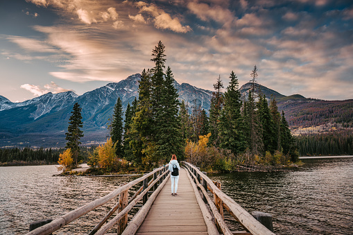 Female tourist standing on wooden bridge and tiny island on Pyramid Lake in the evening at Jasper national park, AB, Canada