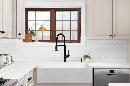 A kitchen faucet detail with a farmhouse sink, black faucet, white subway tile backsplash, and a wood framed window.