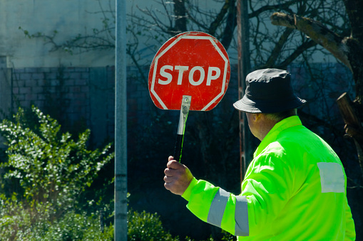 A Coruña, Spain - April 6, 2022: Worker holding stop road sign in urban road wearing reflective working clothes and rain hat, road works ahead, Copy space on the right. A Coruña province, Galicia, Spain.