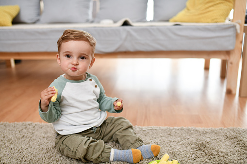 Smiling Baby Boy Chewing Favorite Snacks While Sitting On Floor