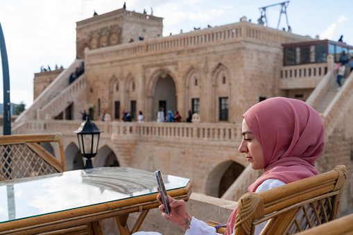 A woman with a headscarf sitting in the view of the stone mansion in Midyat district of Mardin province. woman is sitting at the table on the terrace. Shot with a full-frame camera on a sunny day.