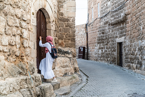 Tourist woman wearing a headscarf walking on the cobbled streets between stone houses in Midyat district of Mardin. Tourist woman wearing a headscarf is walking around the historic stone streets. going up the stone stairs leading to the mansion. Shot with a full-frame camera in daylight.