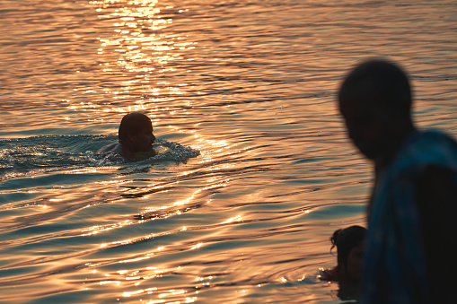 Babughat, Kolkata, 06/11/2023: Silhouette of people bathing in Ganges in a hot summer day. The river Ganges is lifeline to millions of Indians and had profound influence on everyday life of people.