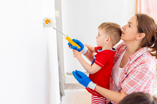 Happy family mother and child son paint the wall with paint using roller and brush. Repair in the apartment