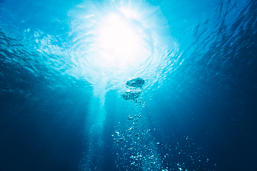 Air bubbles rising to the surface with light rays from scuba diving in the ocean.