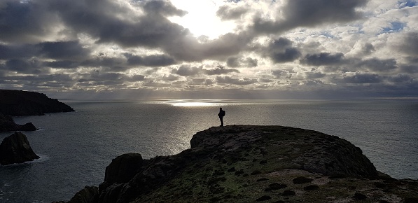 A man stands on the edge of a cliff with a beautiful seascape in the background. Bristol Channel, UK.