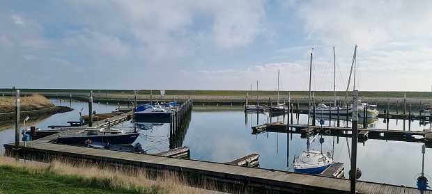 Houseboats moored in the marshes at Felixstowe Ferry in Suffolk, Eastern England, with a boatyard behind and in the distance the village of Bawdsey across the River Deben estuary on a sunny day in springtime. Several of the houseboats are reached via a long walkway on stilts, a necessity at high tide.