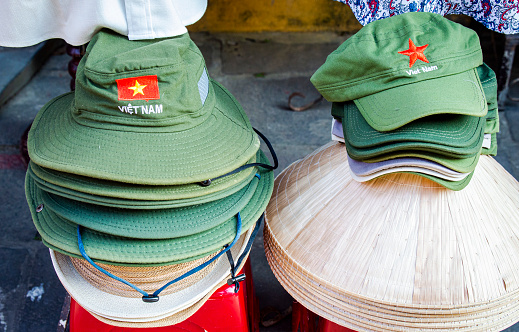 Rice hats and green fabric hats stacked for tourists in Vietnam street, hat showing the word \