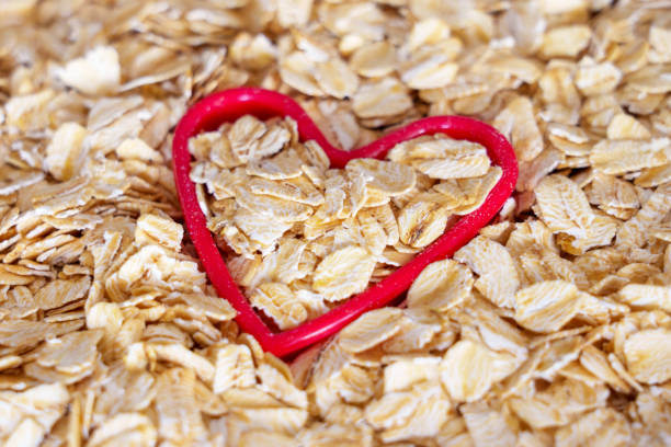 ungekochte gerollte haferflockensamen in roter herzform - oatmeal oat heart shape rolled oats stock-fotos und bilder