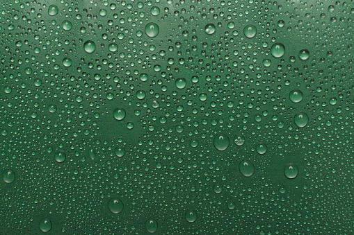 Close-up of raindrops on glass with teal tone, feeling clammy.